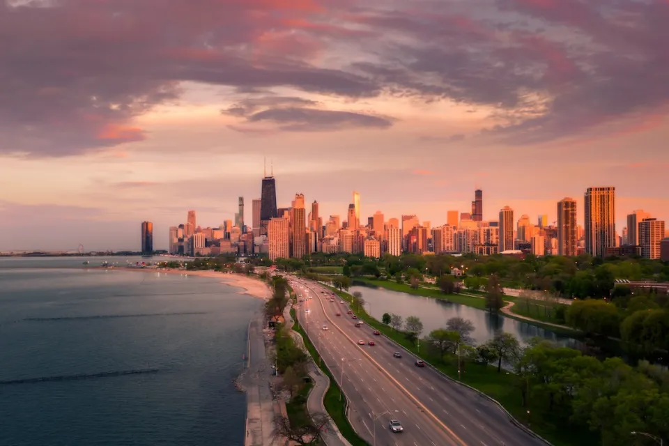 Aerial view of Lake Shore Drive, eight-lane highway adjacent to lakeshore in Chicago, Illinois with city skyline in background at sunset.